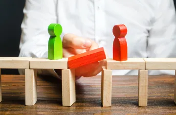 Bridge built out of blocks with two block figures on either side with a hand holding the middle block of bridge